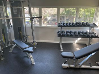 A gym with weights and chairs and a window